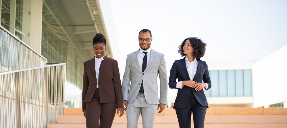 Happy businesspeople walking near office building. Team of business man and women going down stairs, talking, laughing. Teamwork concept
